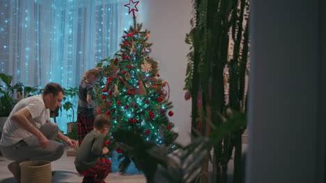 The-family-decorates-the-Christmas-tree-together.-The-father-is-a-mother-and-two-children-put-on-Christmas-trees-together.-Happy-family-on-Christmas-Eve.-High-quality-4k-footage